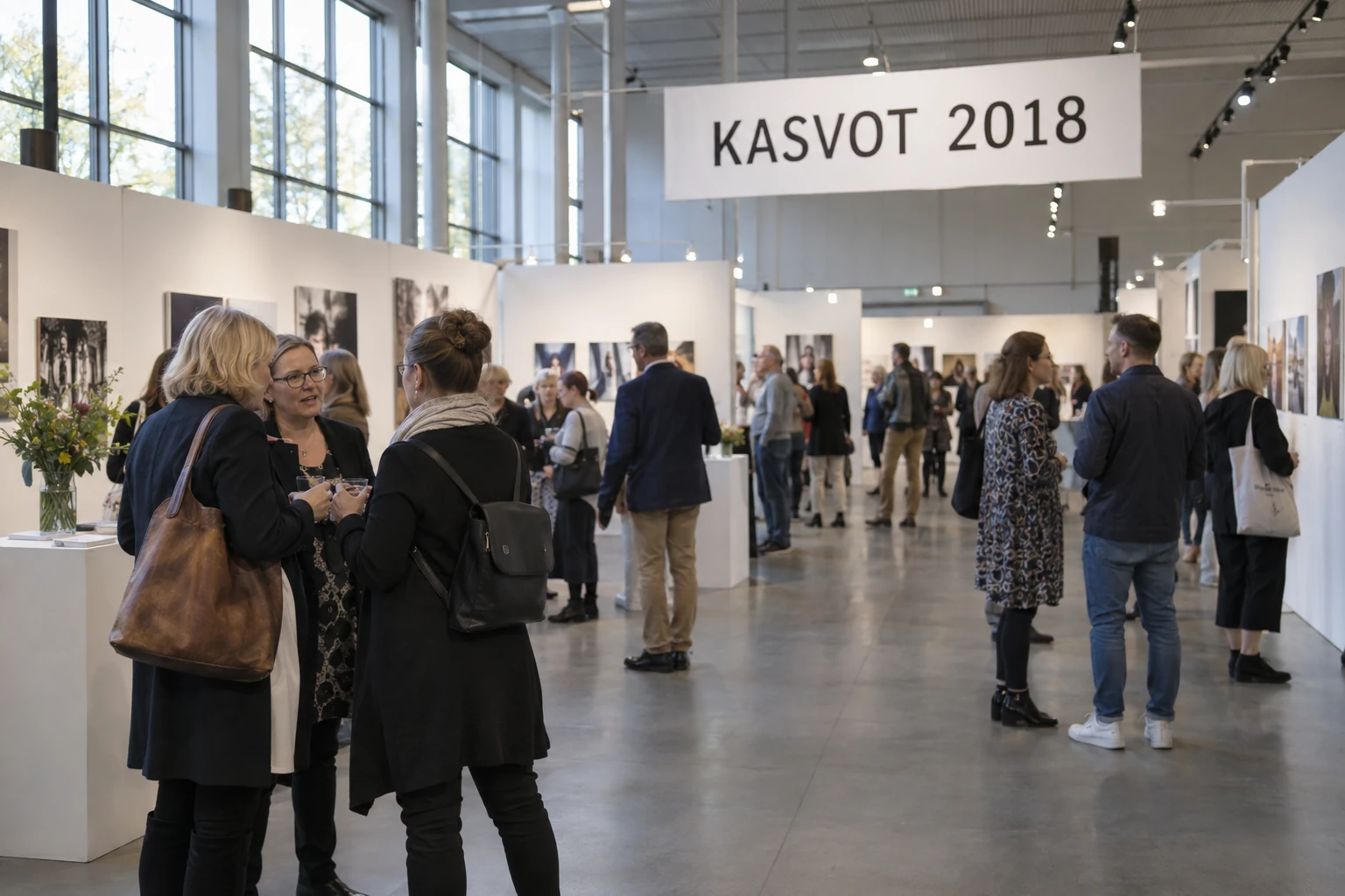 Yleisöä valokuvanäyttelyssä KASVOT 2018 -kyltin alla.